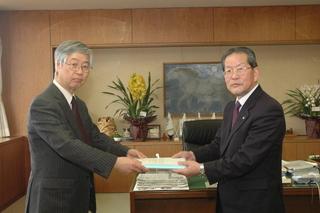 二人のスーツを着た男性が書類を手渡ししている写真
