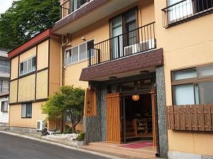 あったか~い宿 勝風館の外観を撮影した写真。建物は道路沿いに面しており、オレンジの外壁となっている。