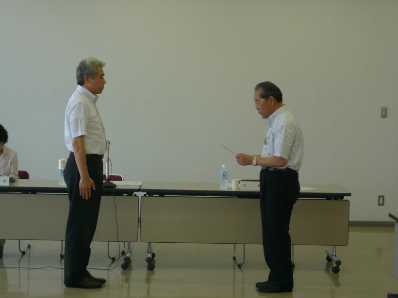 長椅子の前で二人向かい合わせに立ち、委員へ委嘱状を交付している写真