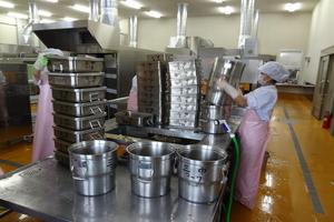 3種類のアルミの食缶を洗浄している3人の白い作業着にピンクのエプロンで身を包んだ職員の写真