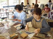 一貫張りのものづくりをしている2人の女性とその後ろのテーブルにも参加者がいる写真