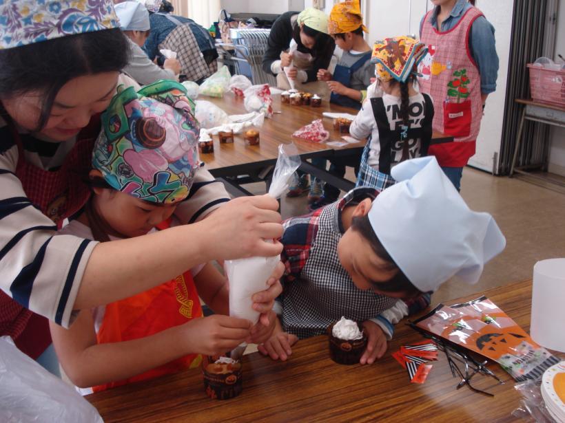 エプロンと三角巾をつけた子どもと親たちが一緒にお菓子作りをしている写真