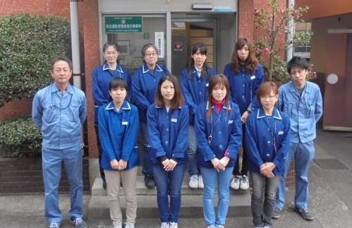 従業員の男女が会社入り口に並んで立っている写真