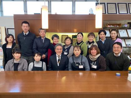 茶色い長机と表彰状などが飾られた室内で横二列に並んでいる施設職員たちの写真