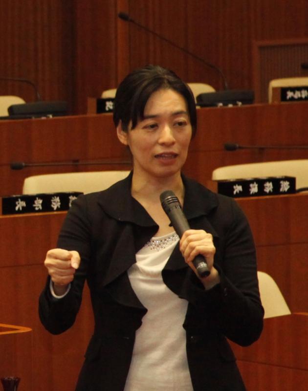マイクを持った黒い服の女性が、議会で話をしている写真