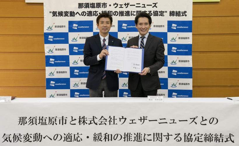 スーツ姿の笑顔の男性二人が契約書を持って立っている写真