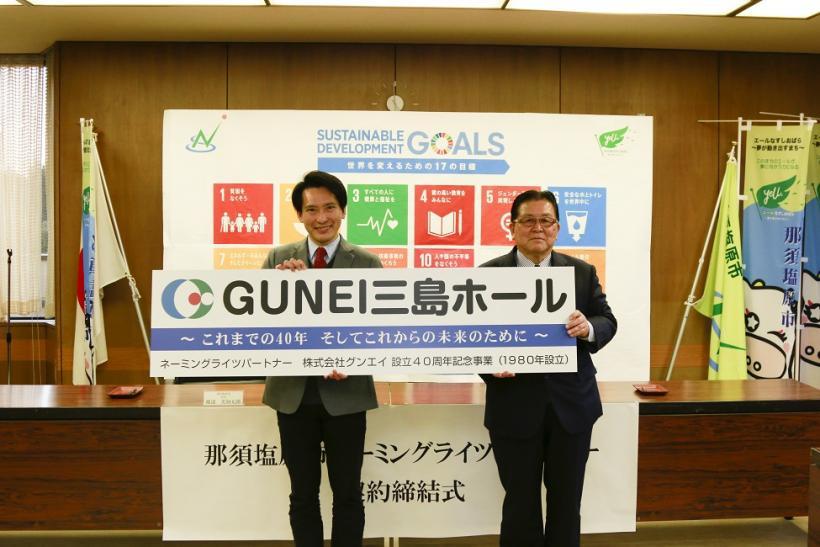 二人の男性が「GUNEI三島ホール」と書かれたプレートを持って並んでいる写真
