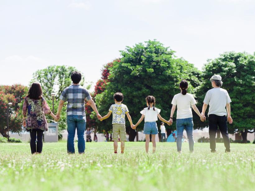 祖父母と親子の6人が芝生に立ち背中を向け手を繋いでいる写真