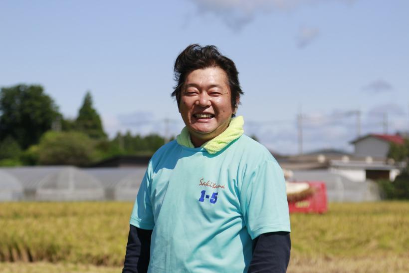 田園の前で笑顔をみせている横山武男さんの写真