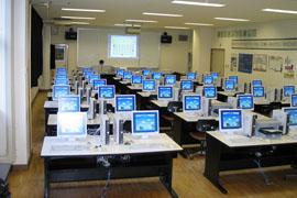 奥にスクリーンのある中で青い画面をしたパソコンと机がたくさん並んでいる澤田書店の内部の写真