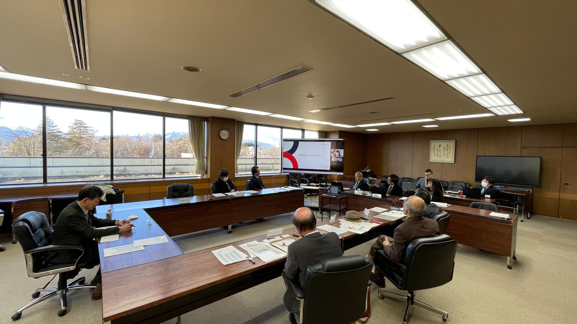 多くの人が長テーブルを四角に囲んで室内で審議会をしている写真