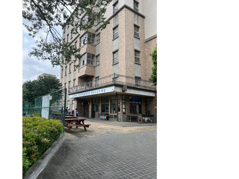 アイビーカレッジエイトアカデミーの茶色いレンガ造りの校舎が写っている写真。手前の広場には、木製のベンチとテーブルが置かれている。