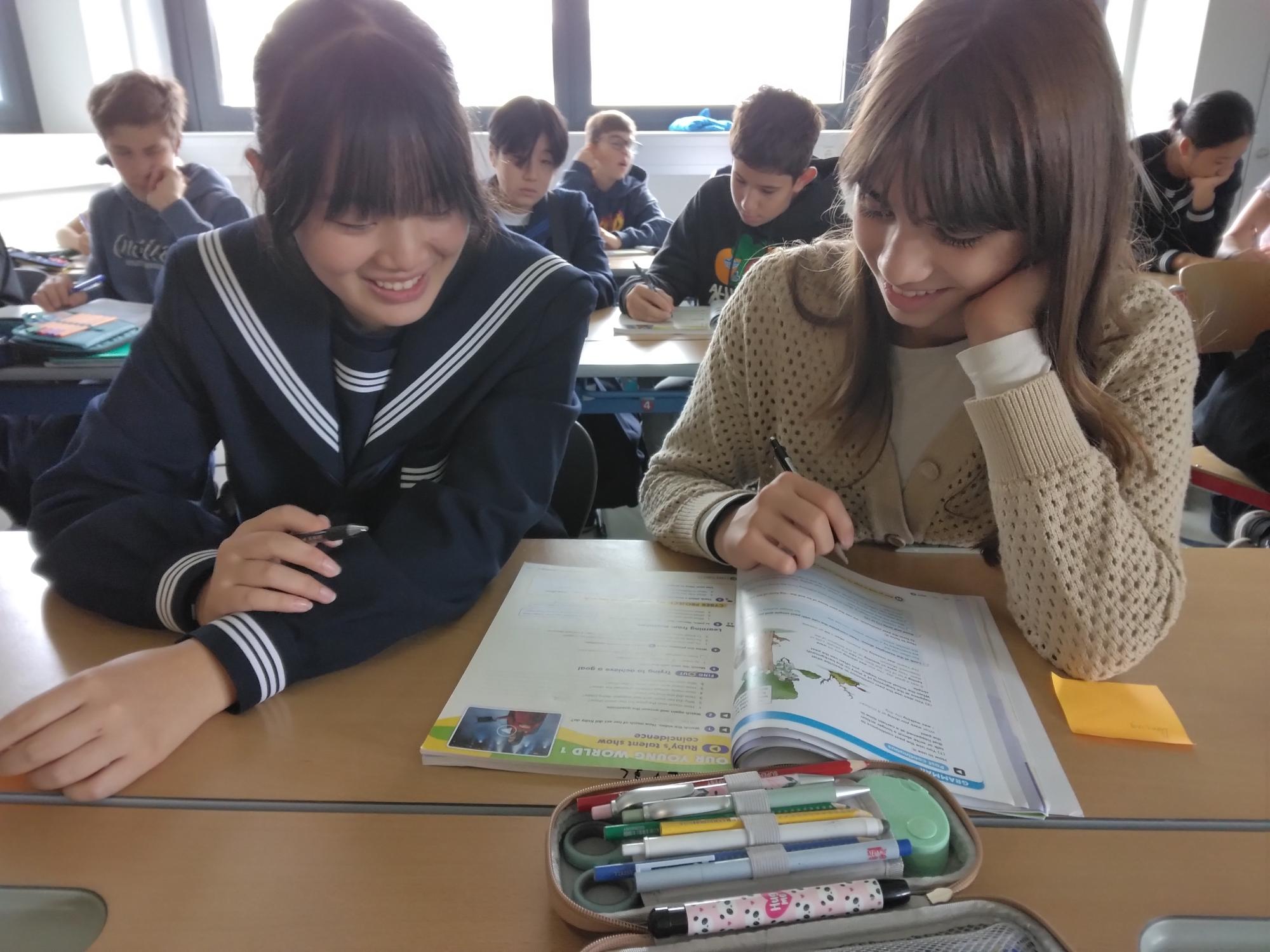 ウホフ校の授業の様子。中学生がアウホフ校の生徒と笑顔で教科書の問題を解いている。