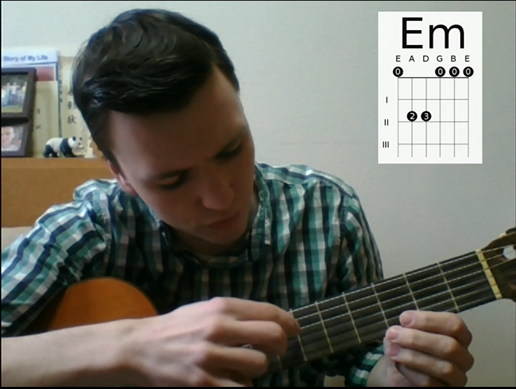 動画の中で、ジェイク先生がギターを持ちながらEマイナーのコードの弦の押さえ方を説明しているシーンを切り取った写真