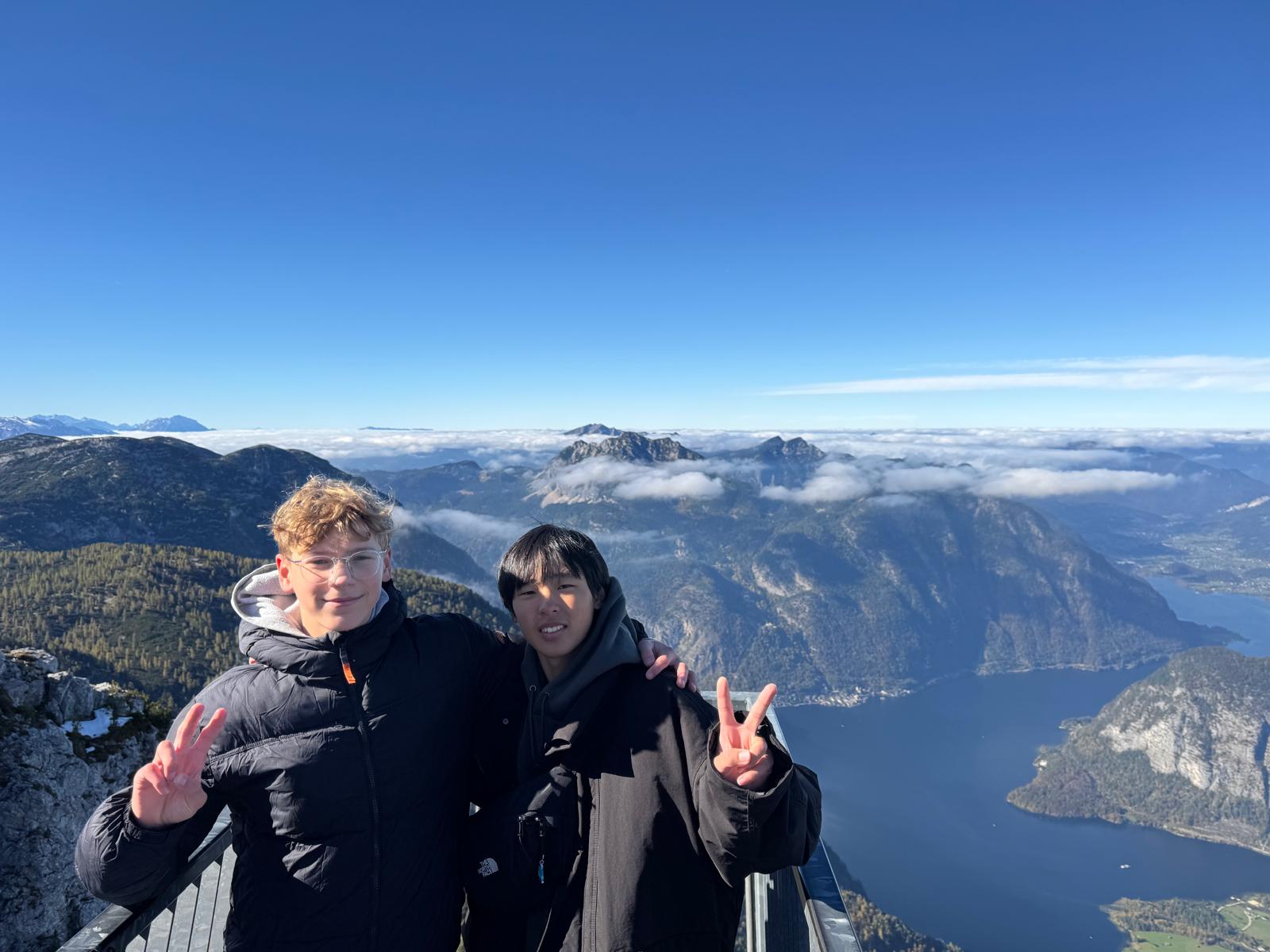 中学生とホストパートナーが肩を組んでいる。二人は高台の場所にいる。背景には山と湖が見える。