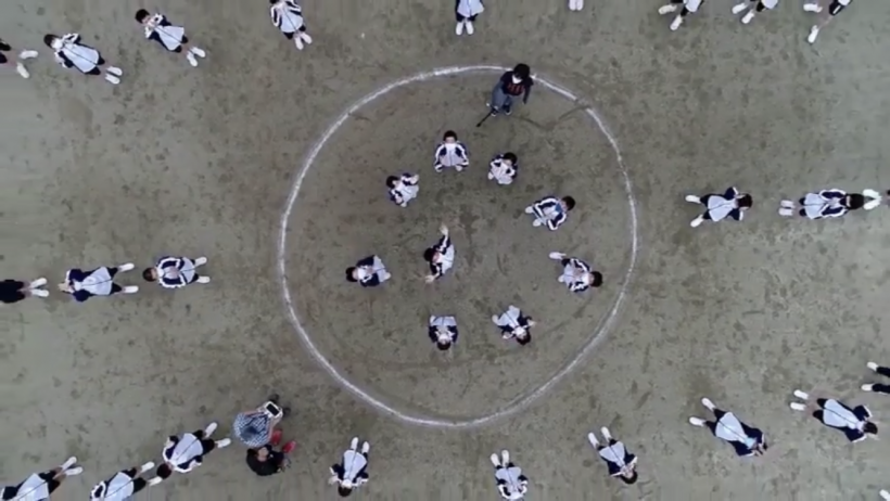 動画「感動の拍手プロジェクト」のサムネイル画像。市内の中学生たちが校庭で拍手の輪をつくる様子を、上空から撮影したカットが確認できる