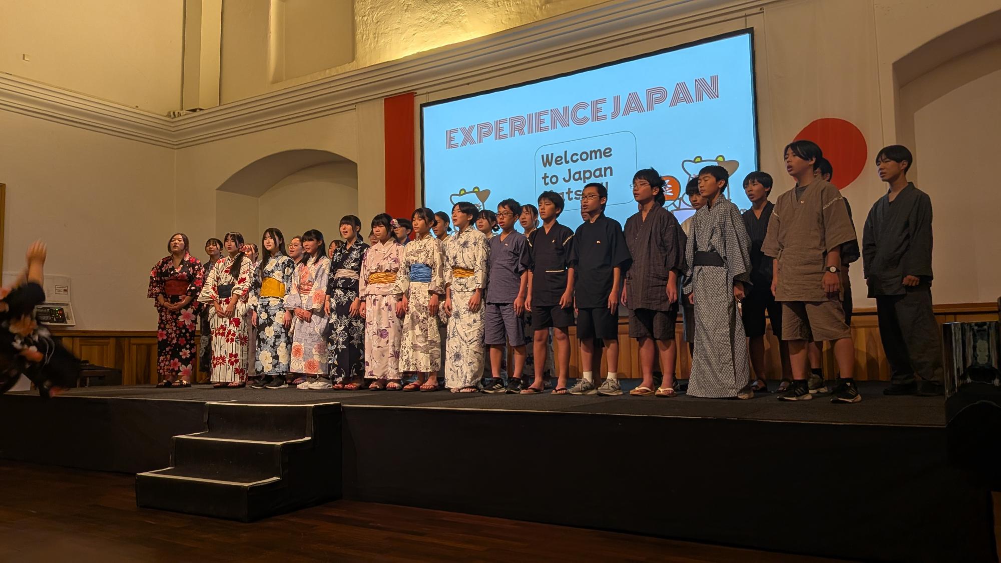 中学生がステージの上で合唱をしている様子。生徒たちは浴衣又は甚平を着ている。