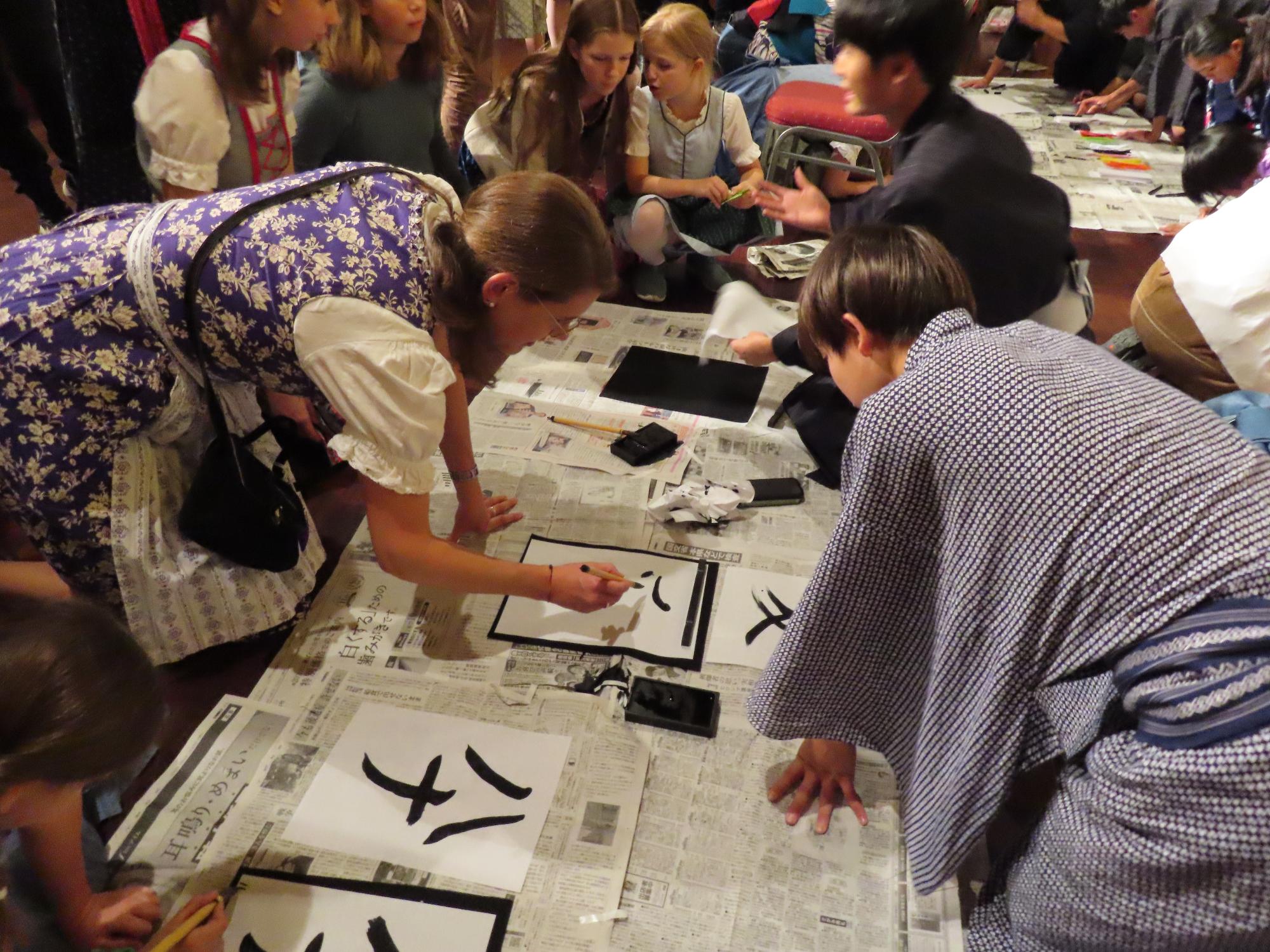ジャパン祭りの文化体験の様子。浴衣を着ている日本人生徒たちはオーストリアのホストファミリーに習字を教えている。