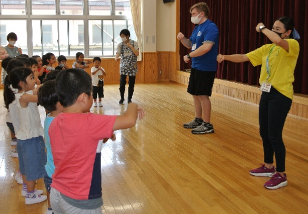 体育館で2人のALTが子供たちと一緒に踊っている写真
