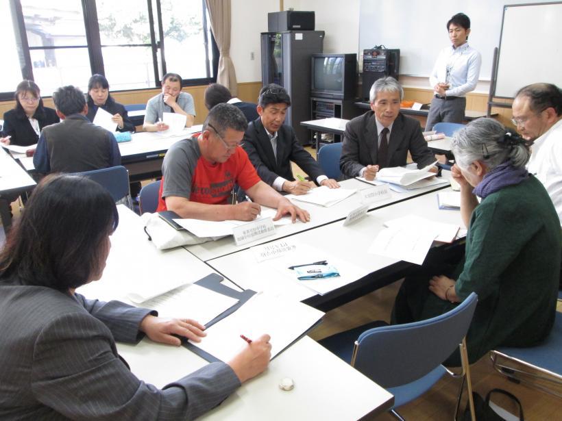私服やスーツ姿の参加者たちが机を囲んで会議をしている写真