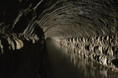 灰色の壁と天井があり下部に水がたまっている西隧道内部の写真