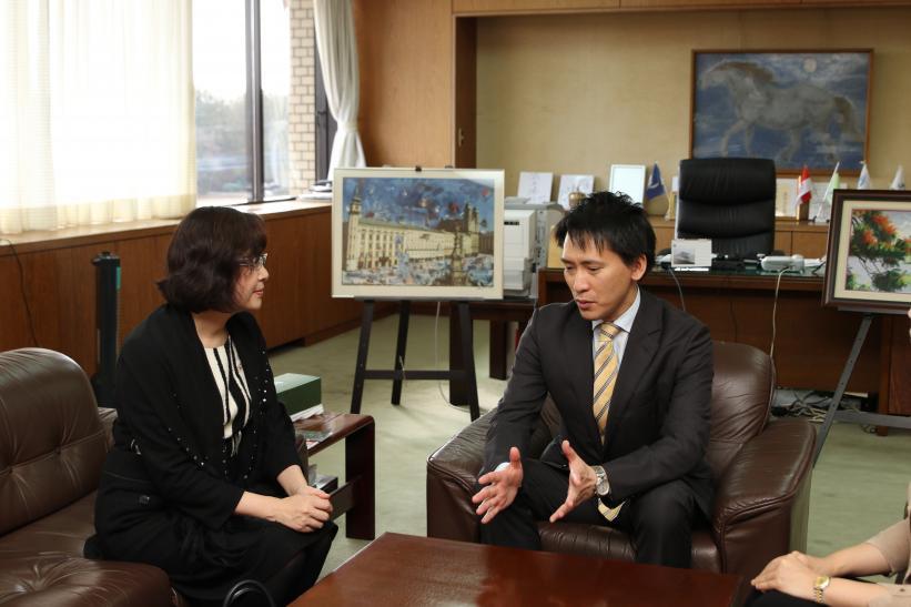 女性と市長が執務室の茶色い椅子に座って会談している写真