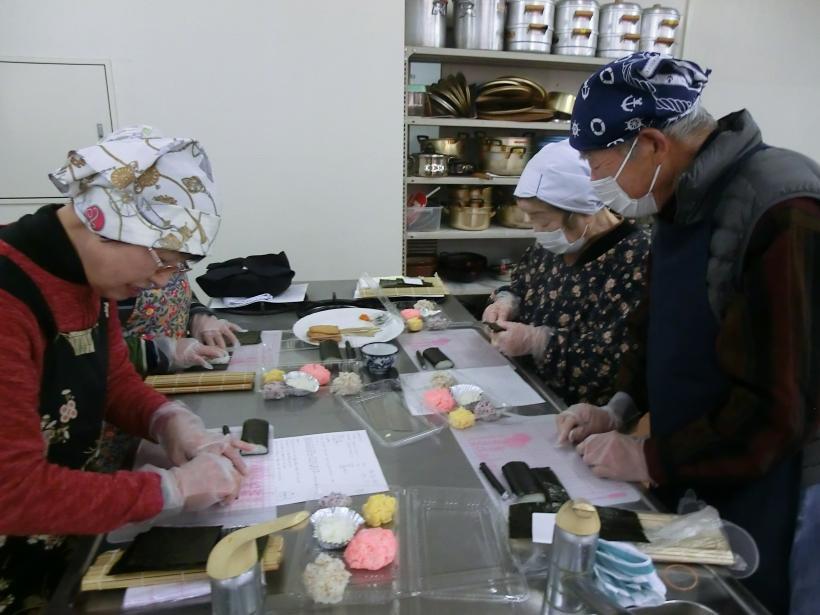 三角巾にマスク姿の参加者が巻き寿司を作っている様子の写真