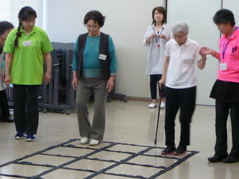 黒い枠の中に足を置いている女性の高齢者とそれを介助する女性スタッフの写真