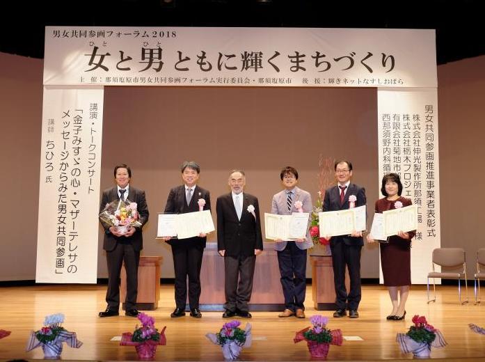 表彰式のステージで男性5人と右端に女性が並んで立っている写真