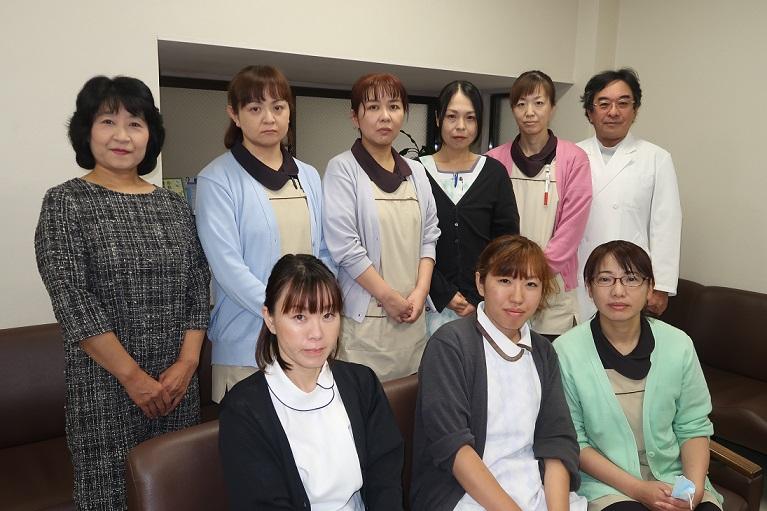 従業員が左斜め前を向いて前列はソファーに座っており後列は立って並んでいる写真