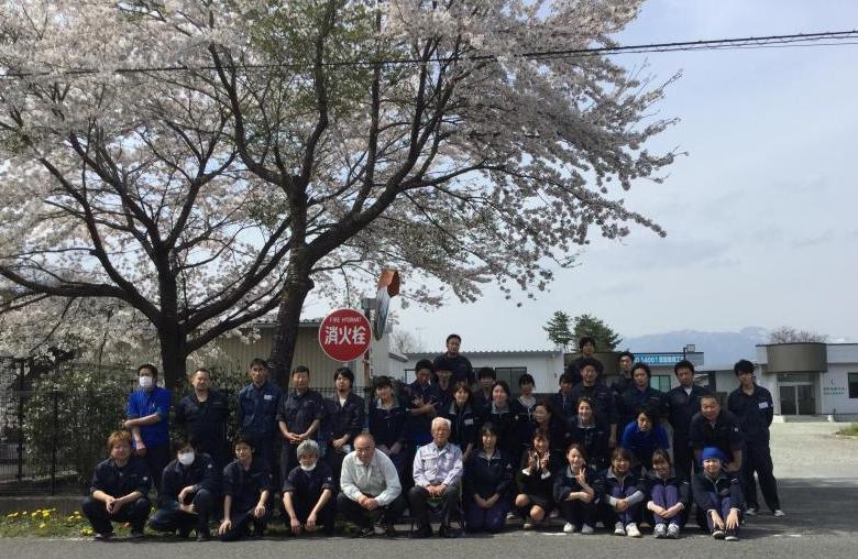 従業員が満開の桜の木の下で前列はしゃがみ後列は立って並んでいる写真