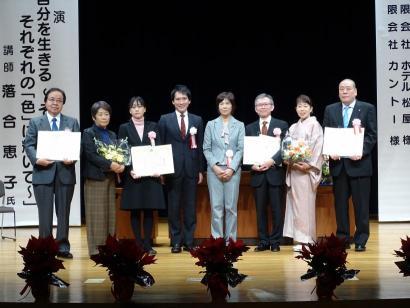 表彰状を持っている8人のスーツ姿の表彰事業者集合写真