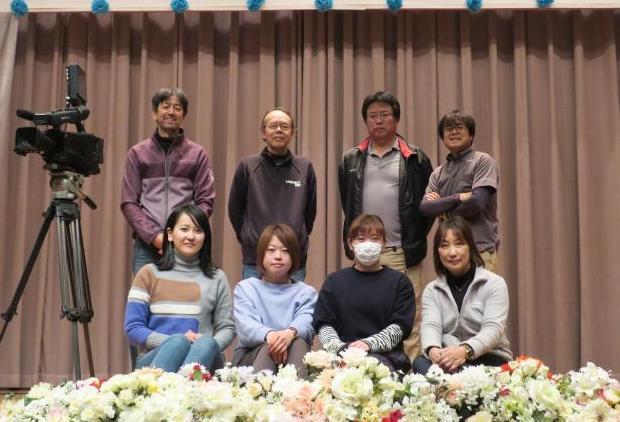 従業員がカーテンの前で男性は後ろに立ち、女性はしゃがんで並んでいる写真