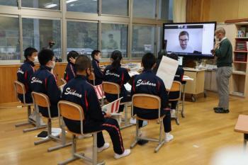 市立塩原小中学校の教室でおこなわれたオンライン交流会において、電子黒板に映し出されたオネア選手と会話する生徒たちを後ろから撮影した写真