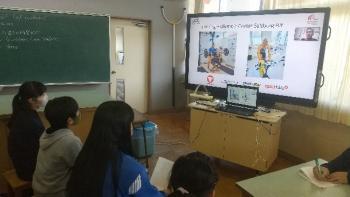 市立東原小学校の特別教室でおこなわれたオンライン交流会において、トレーニング中のマルツィンケ選手の写真を映し出している電子黒板を見る児童たちを後ろから撮影した写真