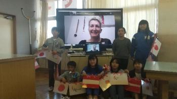 市立東原小学校の特別教室でおこなわれたオンライン交流会において、日本やオーストリアの国旗を持ちながらマルツィンケ選手を映し出した電子黒板を囲んで記念撮影をする児童たちの写真