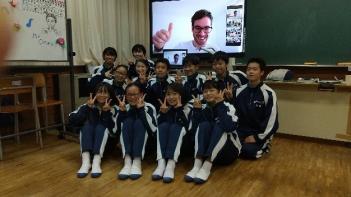 市立東那須野中学校の教室でおこなわれたオンライン交流会において、電子黒板に映し出されたオネア選手の前でブイサインをしながら記念撮影をする生徒たちの写真