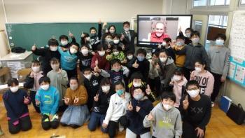 市立埼玉小学校の教室でおこなわれたオンライン交流会において、電子黒板に映し出されたシャッタウアー選手とともに記念撮影をする6年1組の児童たちの写真