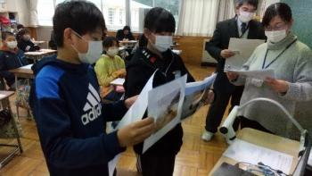 市立西小学校の教室でおこなわれたオンライン交流会において、通信機材である電子黒板の前で写真を使いながら日本のことを紹介する児童たちの写真