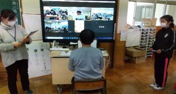 市立西小学校の教室でおこなわれたオンライン交流会において、通信機材である電子黒板の前に置かれた椅子に座って発表をおこなう児童の写真