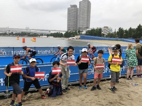 お台場海浜公園の会場へ応援に駆け付けた、市長と子供たちの写真。各々の手にはラミネート加工されたオーストリアの国旗を持つ様子が確認できる