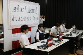 市立東那須野中学校の教室でおこなわれたオンライン交流会において、長机の席に並ぶ生徒たちの写真。背後の衝立には、ようこそ、オネア選手、とドイツ語で書かれている。