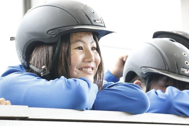 乗馬用ヘルメットを被りつつ、笑顔で見学する児童の写真