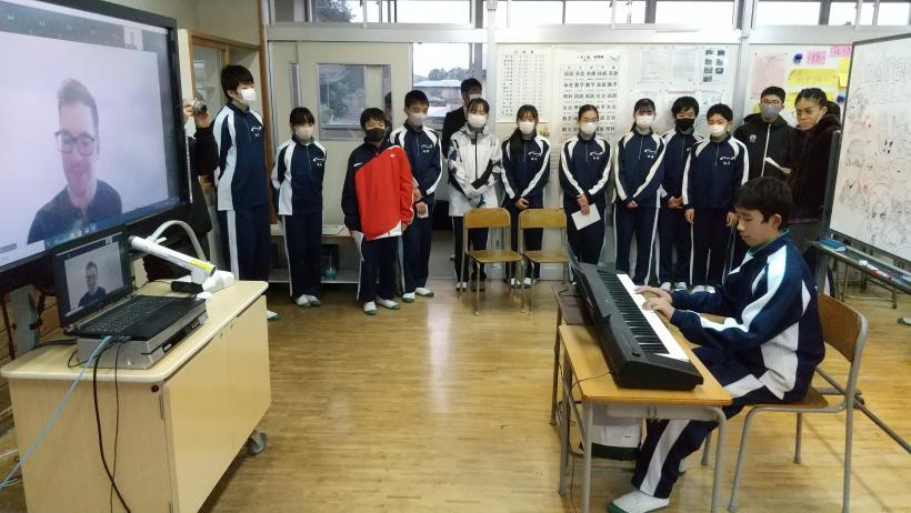 市立東那須野中学校でのオンライン交流会にて、教室に置かれた電子黒板を介してオネア選手に電子ピアノを生演奏する生徒の写真