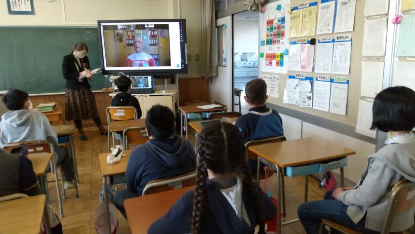 市立東小学校でのオンライン交流会にて、教室の廊下側隅に置かれた電子黒板に映し出されたアブリンガー選手を見る児童たちの写真