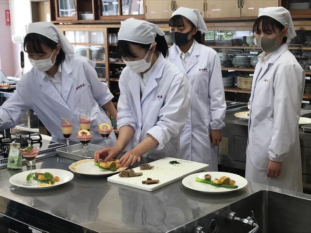 那須拓陽高校の調理実習室にて、出来上がった挽肉や野菜を使ったパイ料理のオニオンタシャルを切り分けて皿に盛り付ける生徒たちの写真