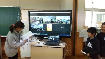 市立西小学校の教室でおこなわれたオンライン交流会において、今回の参加者たちが分割画面で表示されている電子黒板の写真。画面にはグリチュ選手も映し出されている。