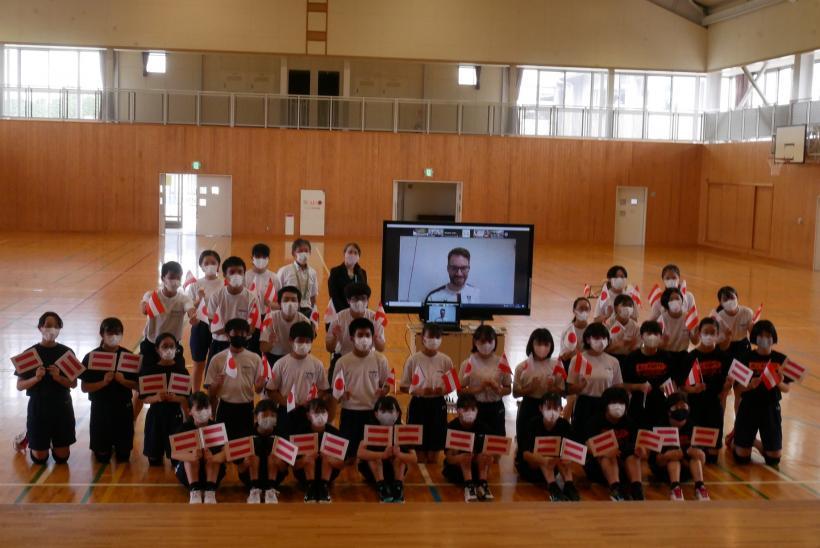 東那須野中学校の体育館にて、オネア選手が映し出された電子黒板とともに記念撮影をする東那須野中学校の生徒たちの写真