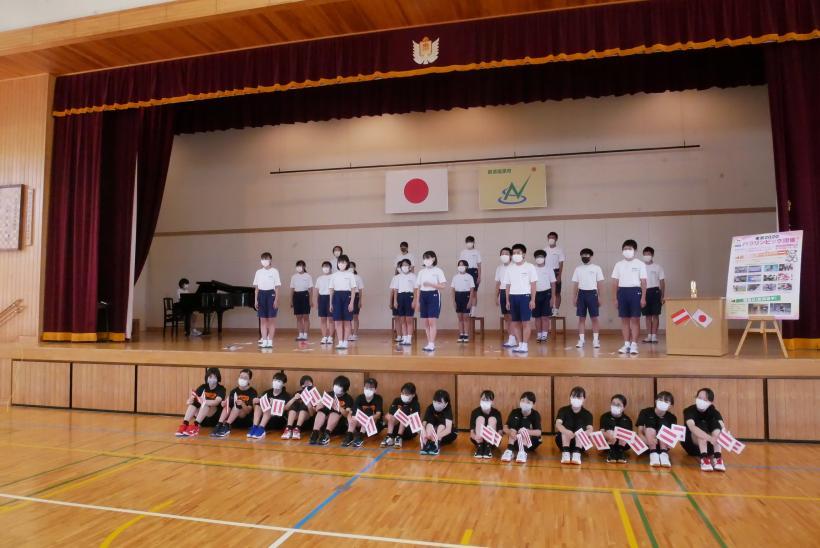 東那須野中学校の体育館で行われたオネア選手交流会で、体育館の壇上にいる生徒たちと壇上の前で体育座りしている生徒たちの写真