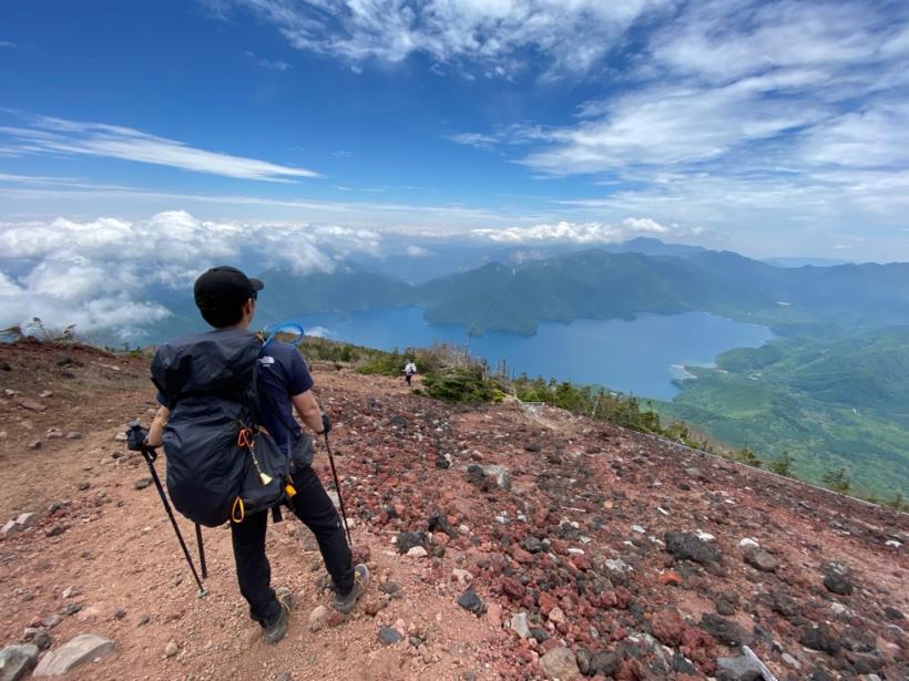 山頂から湖を眺められる絶景スポットに立つ男性の写真